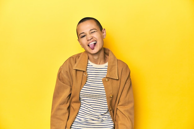 Photo woman in striped tee and denim shirt yellow backdrop funny and friendly sticking out tongue