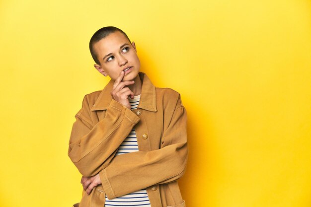 Photo woman in striped tee and denim shirt yellow backdrop looking sideways