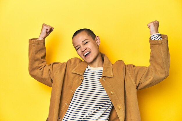 Photo woman in striped tee and denim shirt yellow backdrop raising fist after a victory winner concept