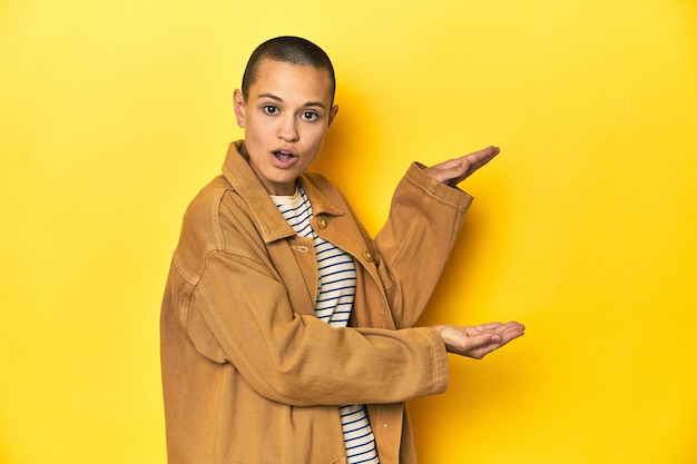 Photo woman in striped tee and denim shirt yellow backdrop shocked and amazed holding