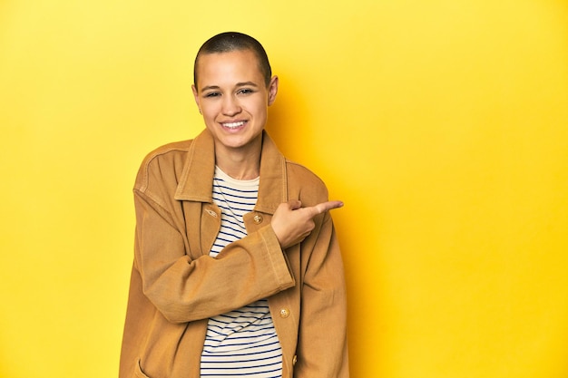 Woman in striped tee and denim shirt yellow backdrop smiling and pointing aside