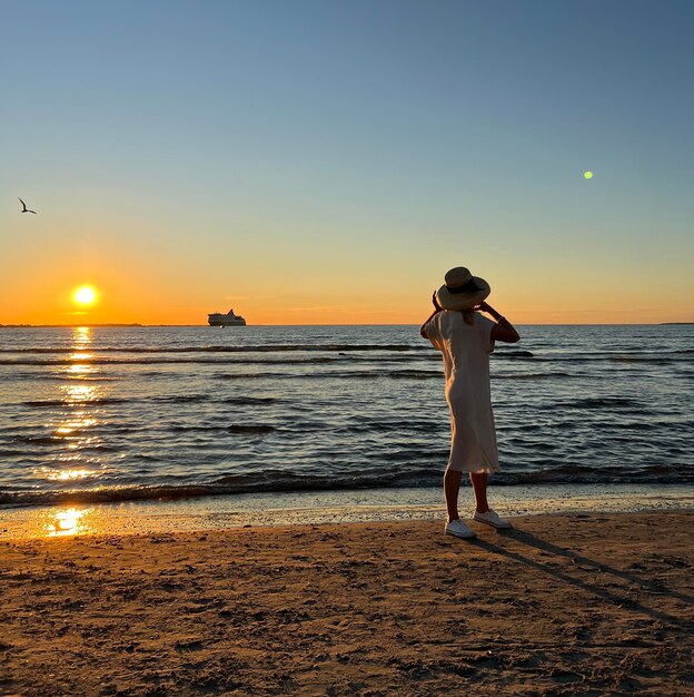 夕日の海でビーチを歩く麦わら帽子の女性