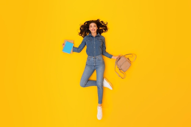 Photo woman student holding backpack and study books on yellow backdrop
