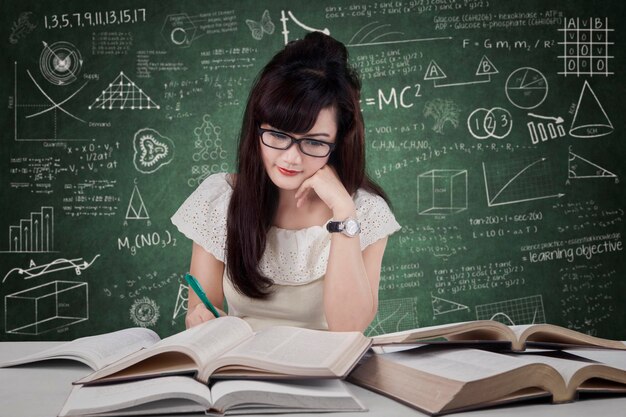 Woman studying while sitting at table against blackboard