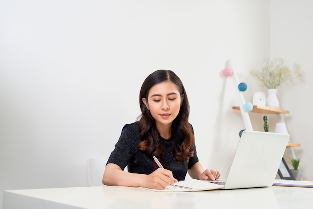 Woman studying with laptop and taking notes on a desktop at home.