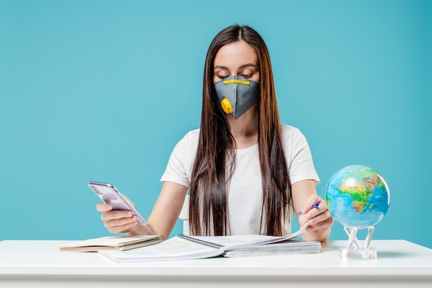 Donna che studia con il globo e il telefono del pianeta terra con i libri che indossano maschera