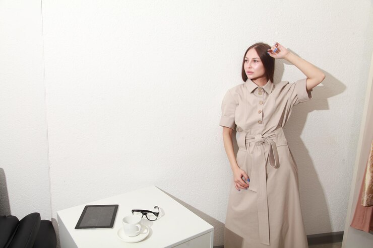 Photo 穿着时尚的<unk>色连衣<unk>的女人站在最简洁的室内远程工作空间的墙上
