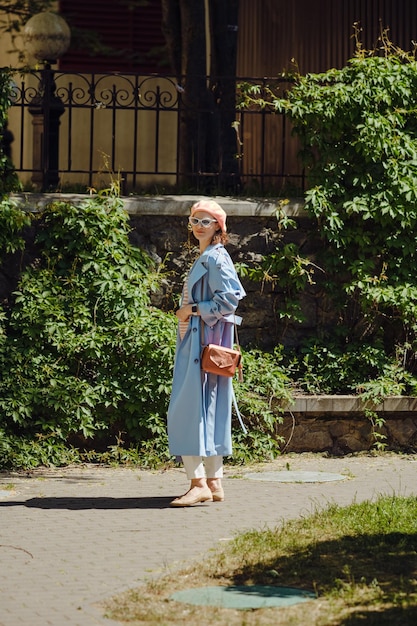 Woman in stylish trendy clothes walking among green foliage