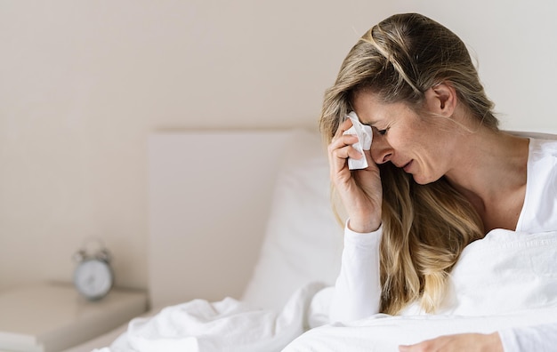 Woman suffering from depression sitting on bed and crying sneezing in tissue sick girl crying at home relationship separation concept image