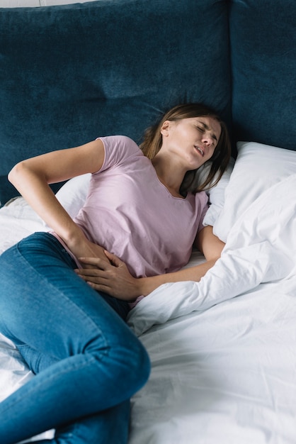 Photo woman suffering from diarrhoea lying on bed