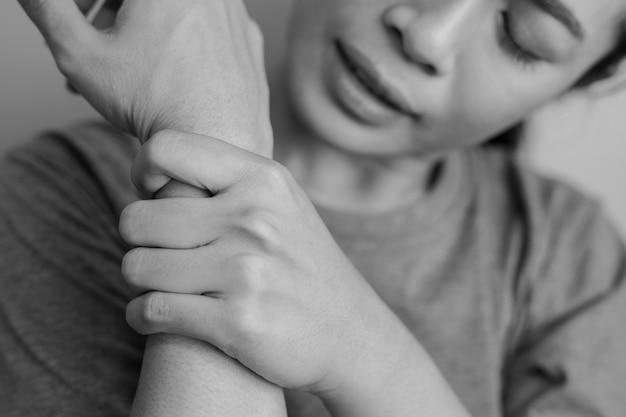 Woman suffering from pain in wrist. pain in a women wrist.\
young woman holding her painful wrist on wall background.