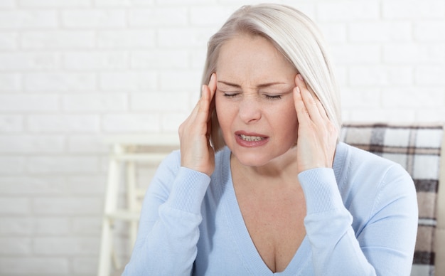 Woman suffering from stress or a headache grimacing in pain as she holds the back of her neck