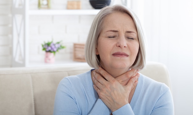 Donna che soffre di stress o mal di testa che fa smorfie di dolore mentre tiene la parte posteriore del collo