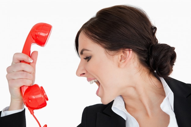 Photo woman in suit shouting against a red dial telephone