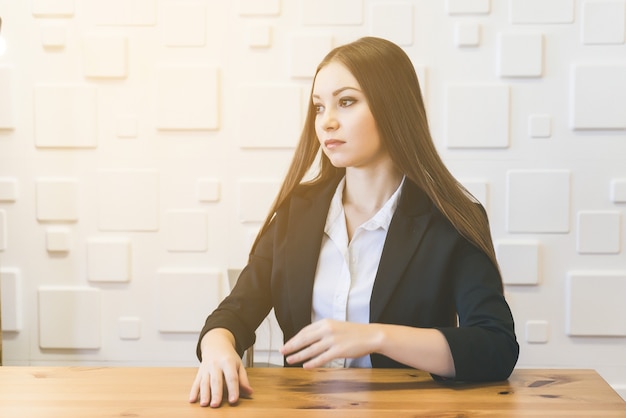 Woman in suit sitting over white wall. Student or teacher on the lecture