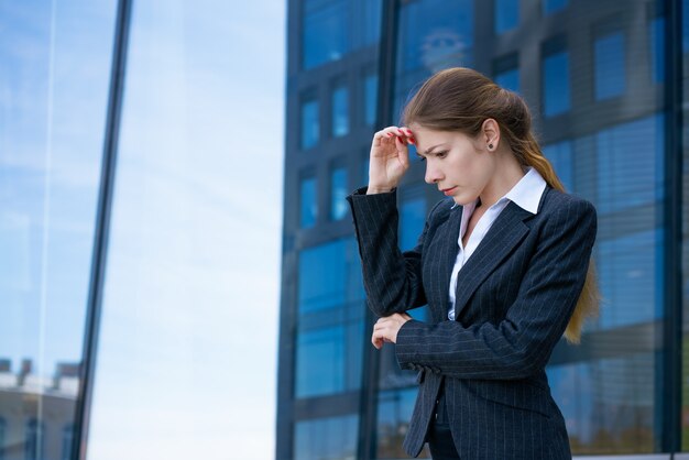 Woman in suit stands thoughtfully on street