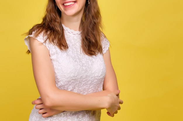 woman in summer clothes stands on yellow and smiles with clasped hands.