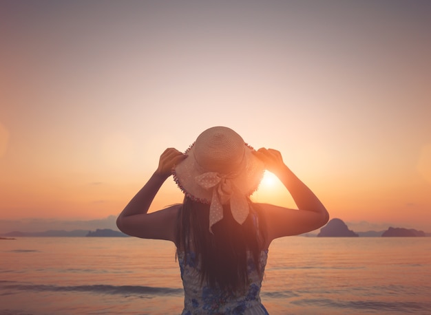 Woman in summer dress standing on a sandy beach during sunset time.