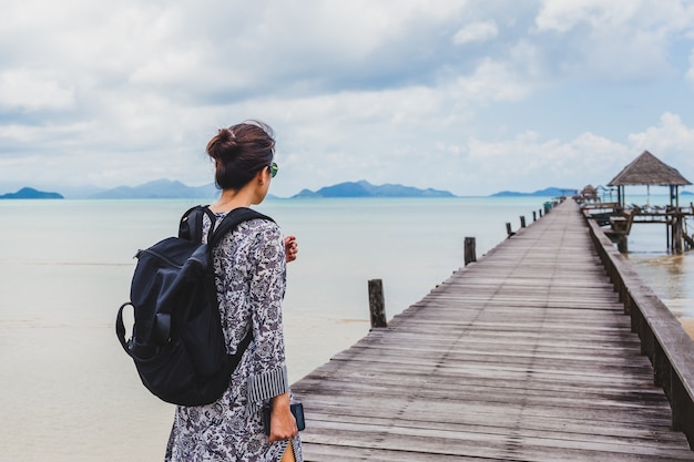 Woman in summer dress walking on wooden bridge with peaceful seascape.