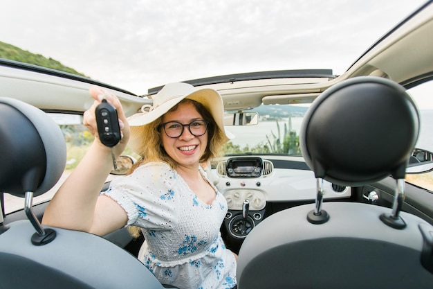 그녀의 새 차 카브리올레 자동차를 운전하는 차 열쇠를 들고 여름 모자 운전사에 있는 여자와 공동 구매