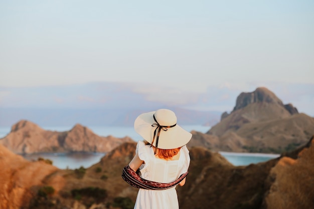 Woman in summer hat and white dress enjoying sea view from top hill on Padar Island