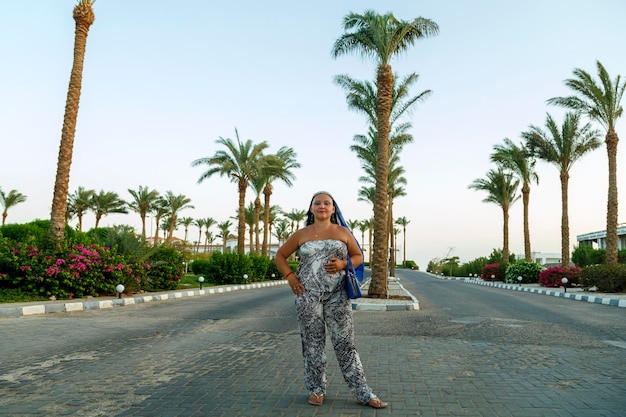 A woman in a summer overalls and a cape on her head on a zhorog among palm trees against