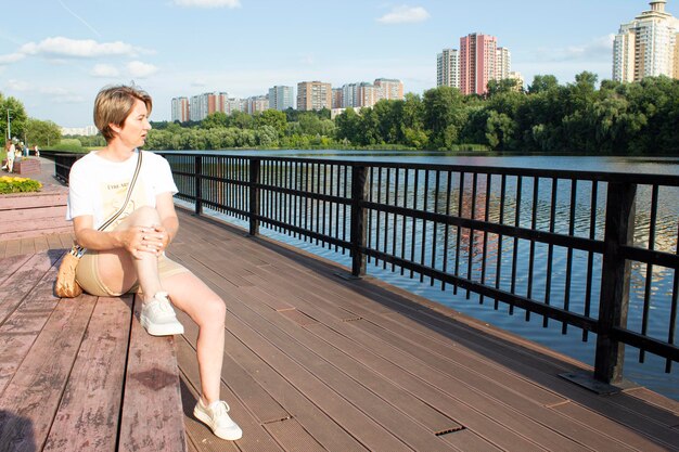 A woman in a summer park is sitting on a bench by the river