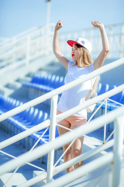 A woman on a summer sports podium in short shorts with bare legs and a cap on her head