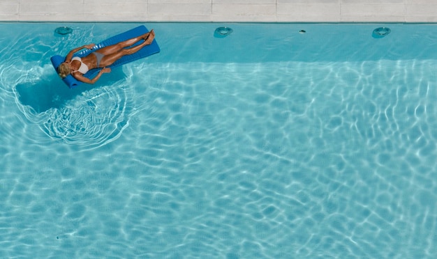 Woman sunbathing in bikini in pool on mat