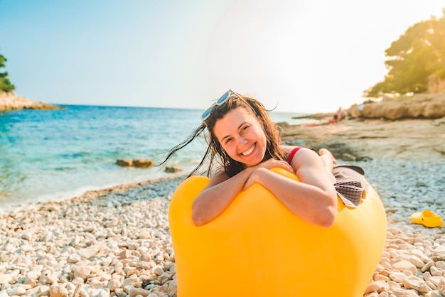 Woman sunbathing at sea beach laying on yellow air sofa copy space