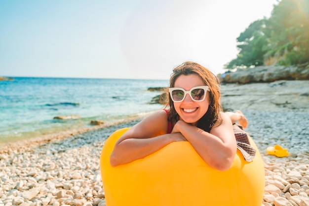 Woman sunbathing at sea beach laying on yellow air sofa copy space