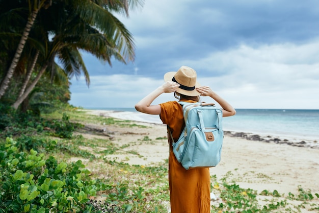 Donna in prendisole e cappello sull'isola vicino agli alberi e lo zaino del mare sullo sfondo