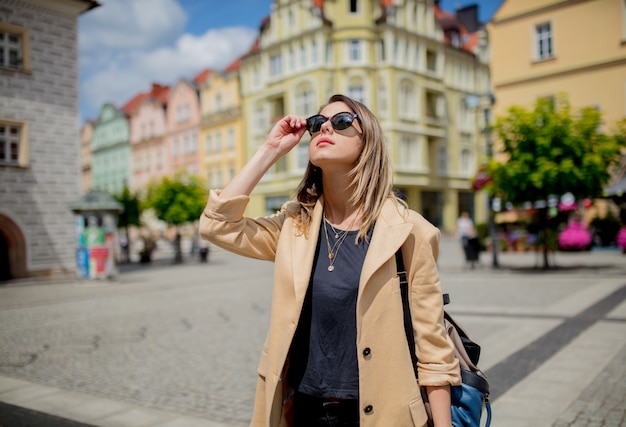 Woman in sunglasses and backpack in aged city center square. Poland