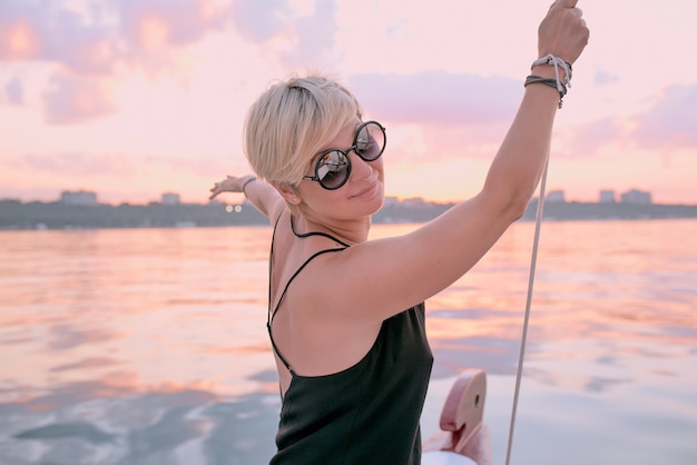 woman in sunglasses and long black dress enjoying sunset on the yacht in the sea