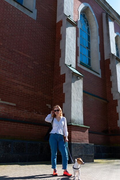 Photo a woman in sunglasses with a dog in the background of a brick house