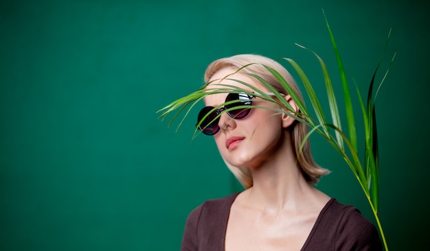 Woman in sunglasses with palm branch on green scene