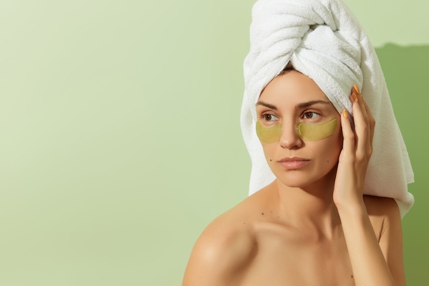 Woman in sunlight with eye patches on pastel green background