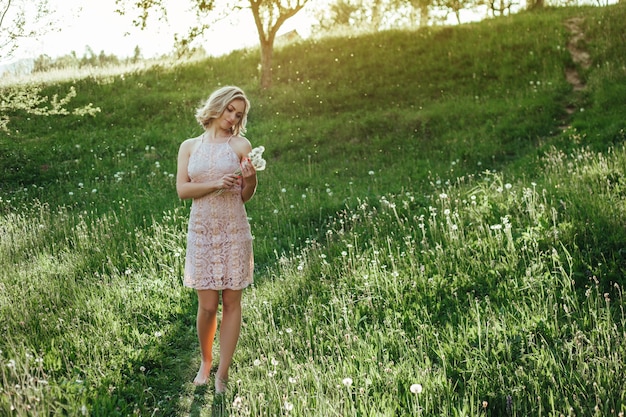 Женщина на закате в поле одуванчиков в розовом платье. концепция не аллергическая.