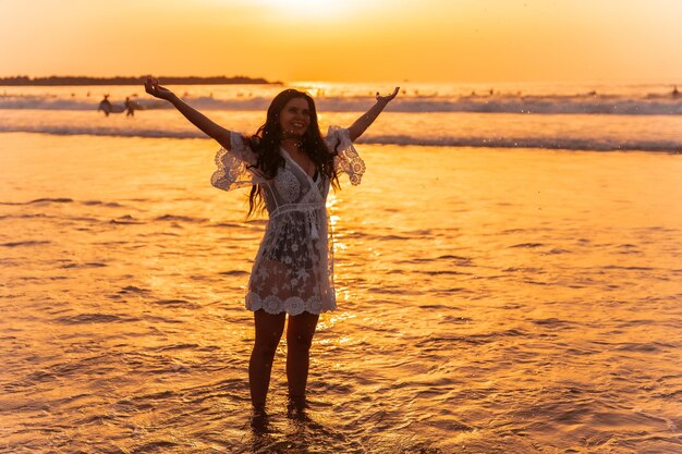 海の水を楽しんでいる白いドレスを着た夕日に映える女