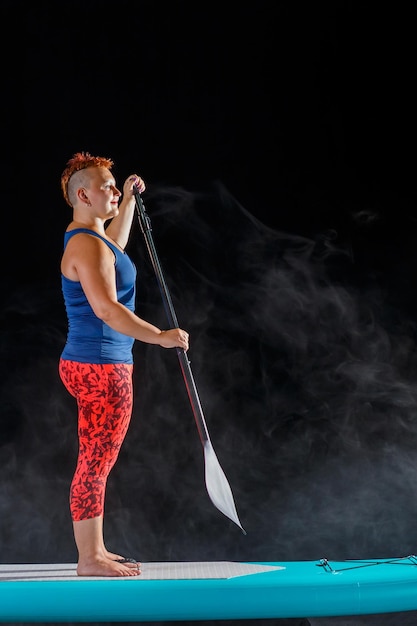 Woman on SUP board with a paddle on a black background