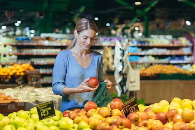 A woman in a supermarket a buyer chooses an apple fruit buys and puts an ecological bag in the