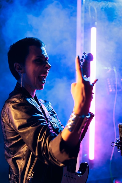 Woman superstar with short hair holding electric guitar playing rock music preparing heavy song to perform at grunge concert. Rockstar in leather jacket adjusting electricinstrument working at electri