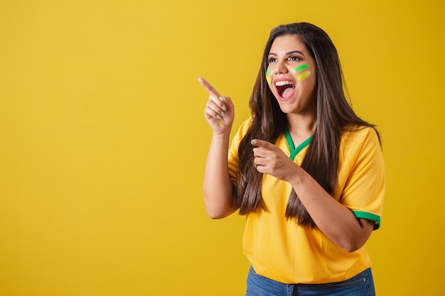 Woman supporter of Brazil world cup 2022 football championship surprised amazing pointing away with fingers to the left