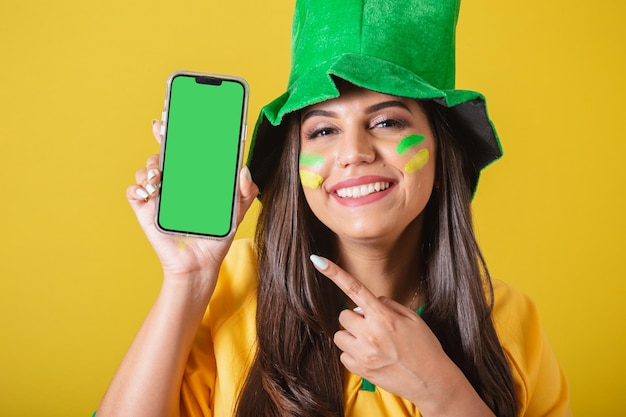 Woman supporter of brazil world cup 2022 holding cell phone\
showing device screen with finger for application and technology\
ads promotions