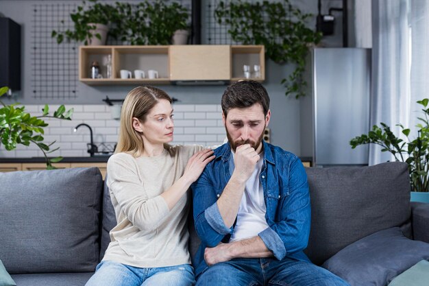 A woman supports an upset husband who has failed a married couple sitting on the couch