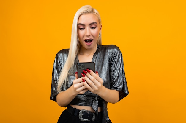 woman in surprise reads messages on her smartphone on a yellow studio background