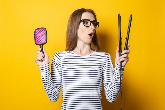 Photo woman surprised shocked holding a comb and curling on a yellow background