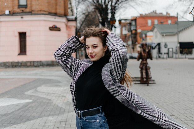 A woman in a sweater and jeans stands on a street