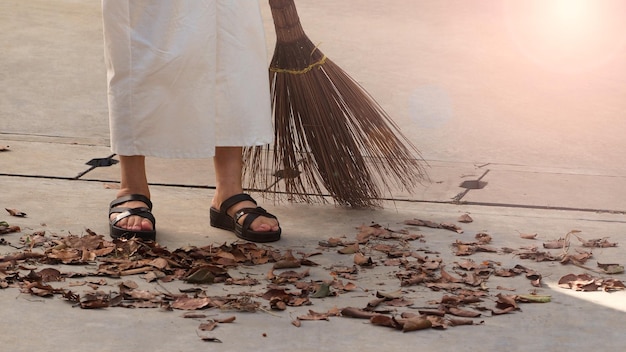 Woman sweeping dry leaves on the cement floor with long wood broom