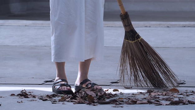長い木のほうきでセメントの床に乾燥した葉を掃除する女性